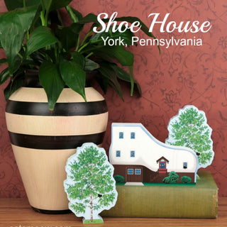Decorative house and tree models with a potted plant on a red background, featuring 'Shoe House' from York, Pennsylvania.