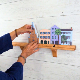 Hand holding a small model of a building on a wooden stand against a white background