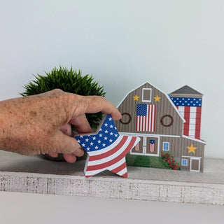 Decorative wooden signs of a barn and a house with American flag designs on a white wooden 