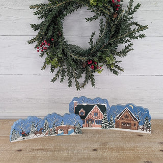 3/4" thick wooden illustration of a horse and carriage in winter grouped with other winter designs on a table with a wreath on the wall