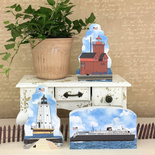 Decorative items including a lighthouse, ship, and small house on a white surface with a plant in the background.