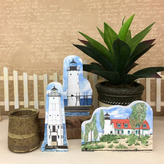 Decorative lighthouse and house signs with a plant on a wooden surface.