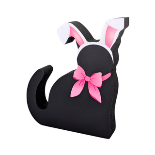 wooden replica black cat that has a pink bow and bunny ears on a white background 