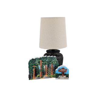 Decorative lamp with a scenic base featuring trees and a sign.