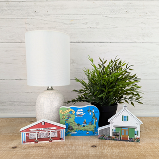 Decorative miniature buildings on a wooden surface with a lamp and plant in the background.