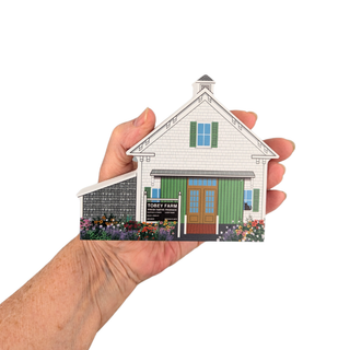 Hand holding a miniature 3/4" thick wooden model of a house with 'Toby's Farm' sign.