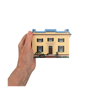 Hand holding a 3/4" thick wooden illustration of a yellow home on a white background
