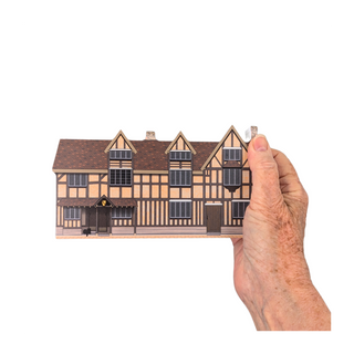 Hand holding a miniature 3/4" thick wooden cutout of a half-timbered house on a white background
