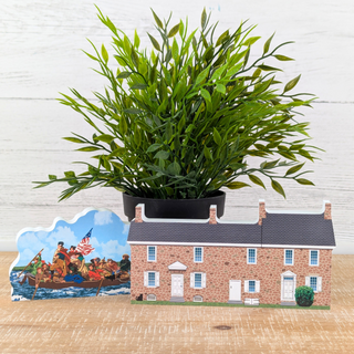 Potted plant on a stand with a historical scene cutout and a brick building model in the background.