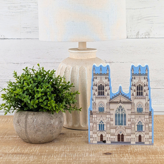 3/4" thick wooden cutout of  a cathedral on a wooden surface with a plant and lamp in the background.