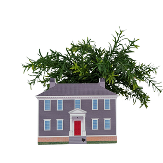 A decorative miniature house-shaped planter with a gray roof and walls, a red front door, white trim, and green artificial foliage growing from the top, shown on a plain white background.