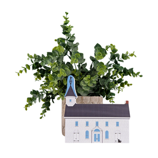 A decorative miniature white church building planter with a blue steeple, holding artificial green eucalyptus foliage, isolated on a white background.