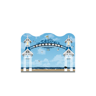 A wooden figurine featuring a stylized illustration of the Boardwalk, Ocean City, MD entrance with white tower structures, a blue sky, beach, and birds.