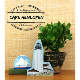 Decorative lighthouse card with a potted plant and book on a wooden surface.