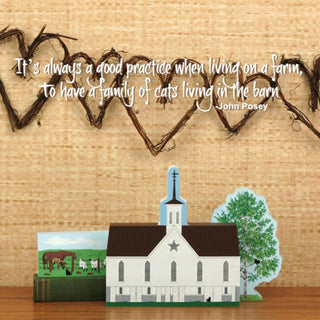 Decorative scene with a small barn model, tree, and farm animals on a wooden surface with a rustic background.