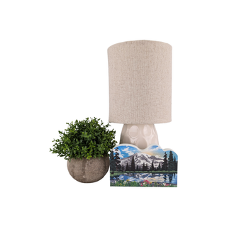 Table lamp with decorative base featuring a mountain scene, next to a potted plant on a white background