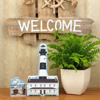 Decorative wooden 'WELCOME' sign with a ship's wheel, lighthouse, and potted plant on a wooden surface.