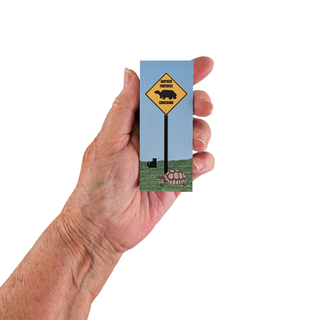 Hand holding a 3/4" wooden replica with an illustration  with a turtle crossing design on a white background