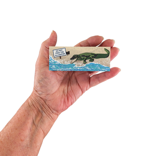 Hand holding a 3/4" wooden replica with an illustration  with an alligator and text on a white background