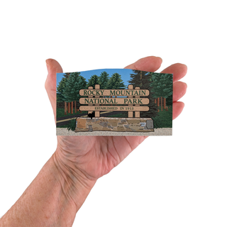 Hand holding a Rocky Mountain National Park replica sign against a white background