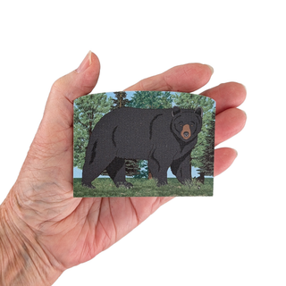 Hand holding a 3/4" thick wooden illustration of a black bear in a forest setting on a white background
