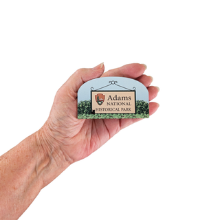 Hand holding a small sign with 'Adams National Historical Park' on a white background