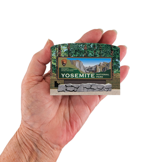 Hand holding a Yosemite National Park wooden replica with a scenic view and park logo.