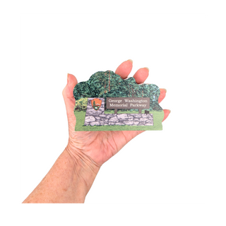 Hand holding a 3/4" thick wooden illustration of a memorial Parkway sign with stone wall and trees on a white background