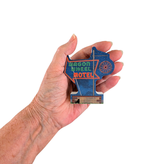 3/4" thick wooden replica with an illustration of a Wagon Wheel Motel' sign shaped like the state of Nebraska, held in a person's hand against a plain white background.