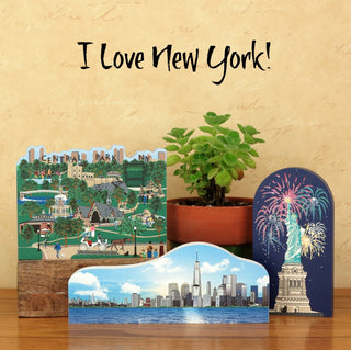 Three decorative 3/4" thick wooden cutous depicting New York City scenes on a wooden surface with a plant in the background.