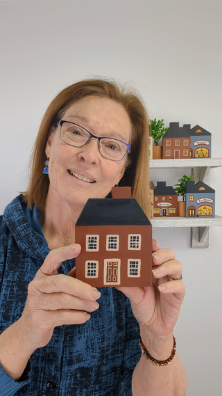 Person holding a small model house with shelves of more model houses in the background