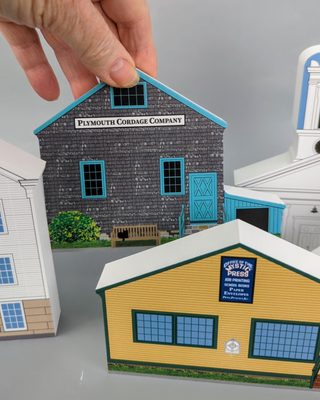 3/4" thick wooden Model of a Plymouth Cordage Company building with a hand holding it against a gray background.