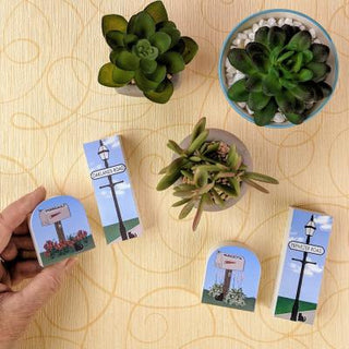 Small decorative signs with street lamp designs on a wooden surface with potted plants.
