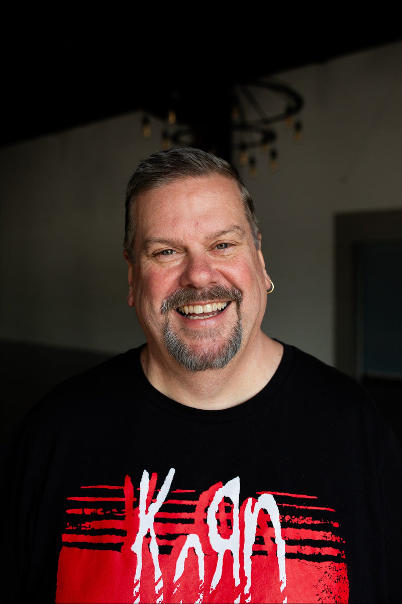 Man wearing a black t-shirt with red and white design, smiling indoors.