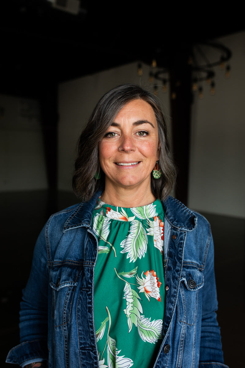 Woman wearing a denim jacket over a green floral dress in an indoor setting