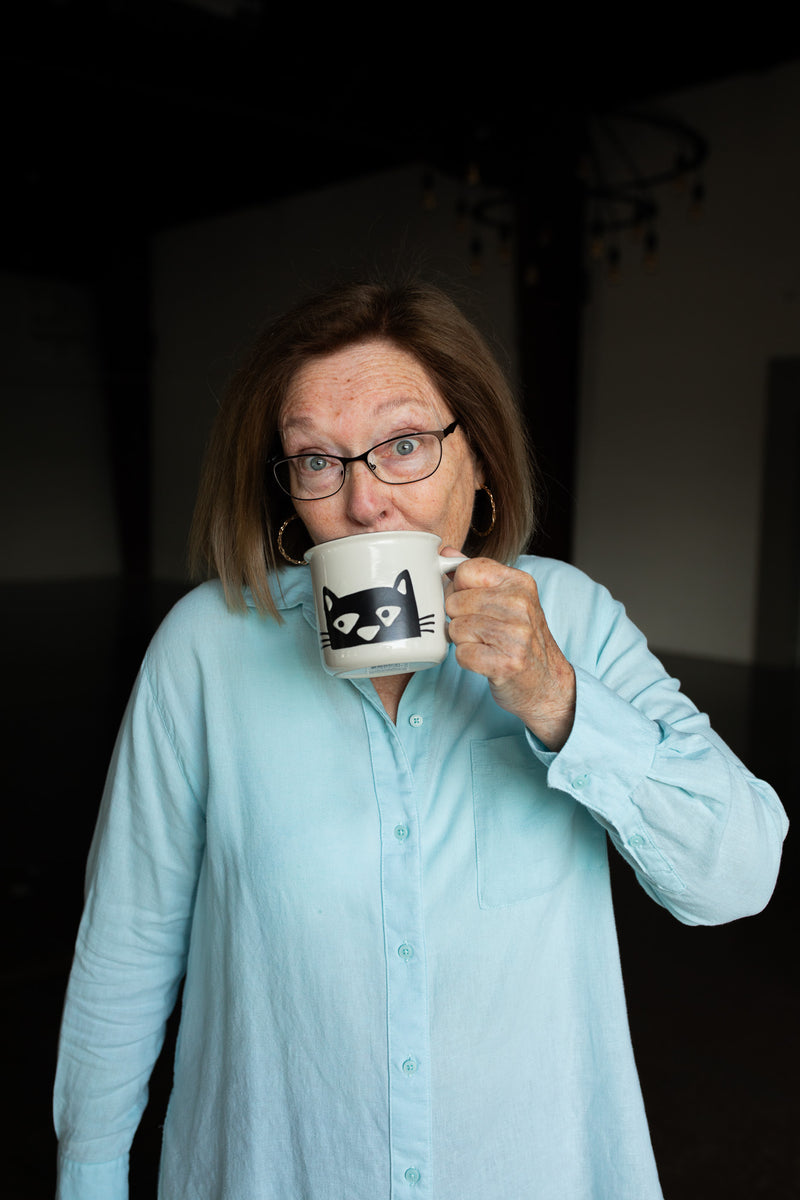 Woman in light blue shirt holding a mug with a cat design against a dark background