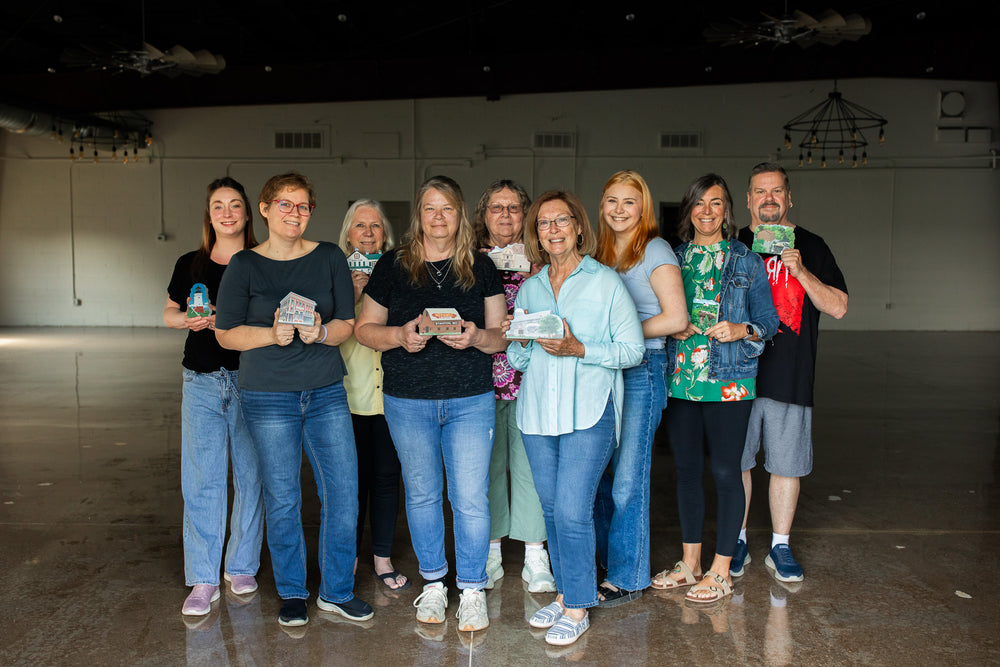 Group of people standing in a large indoor space, holding small green boxes.