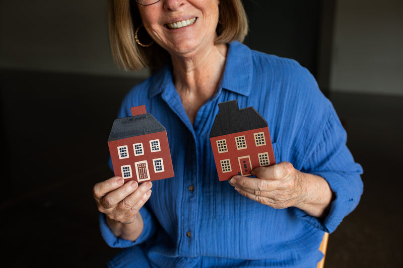 Woman holding two small model houses against a dark background