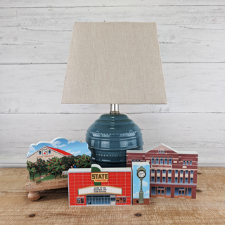 Blue lamp with beige shade on a wooden surface with decorative items.