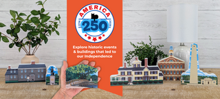 Book titled 'Explore America 250' with model buildings on a wooden surface.