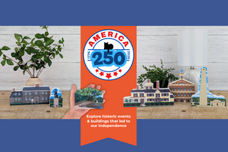 promotional banner for 'America 250' held by a hand with model buildings and plants on a wooden surface.