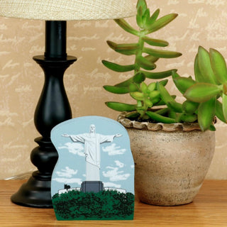Black lamp, potted plant, and small card with a statue of Christ the Redeemer on a wooden surface.