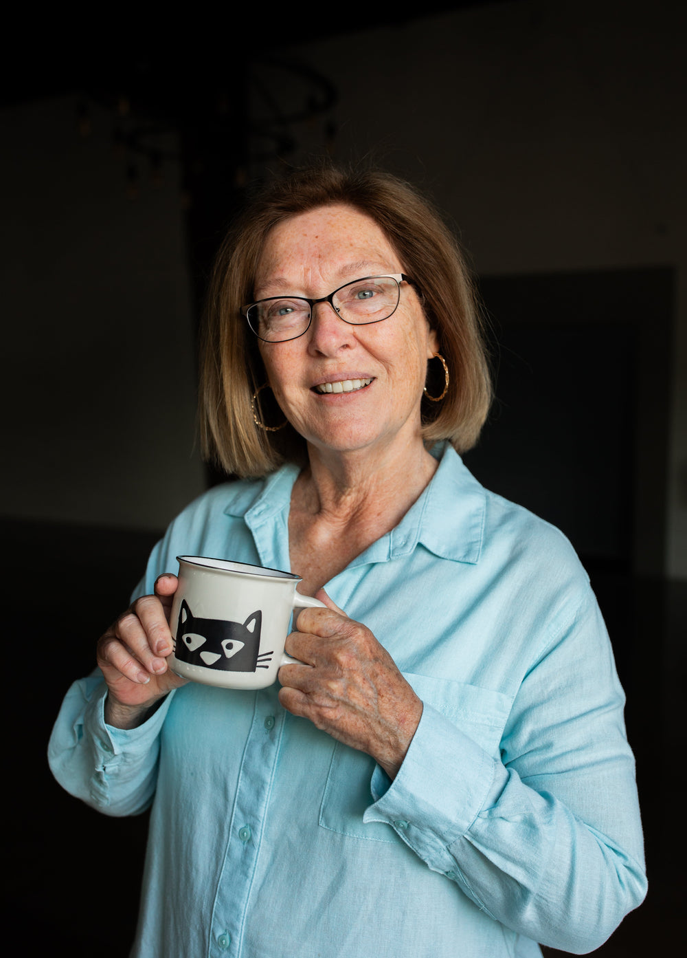 Woman holding a mug with a cat design in a dimly lit room