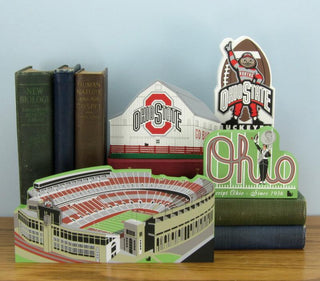 Collection of Ohio State-themed items including a stadium model, books, and a cutout sign on a wooden surface.