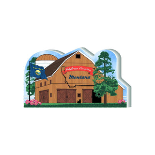 3/4" thick wooden barn with Montana flag and 'Celebrate America' sign, surrounded by trees and flowers.