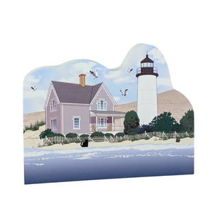 Wooden replica of a lighthouse and house with birds flying in the sky.
