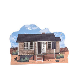 wooden replica with an Illustration of a small house on beach with a blue sky and clouds in the background