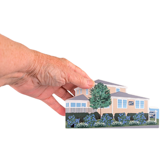 hand holding a 3/4" thick wooden figurine of a yellow house on white background