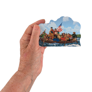 Hand holding a small 3/4" thick wooden cutout of a painting with people in a boat and an American flag.