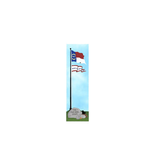 3/4" thick wooden cutout of the North Carolina state flag on a pole with a gray stone and cartoon dog in the foreground against a blue sky.